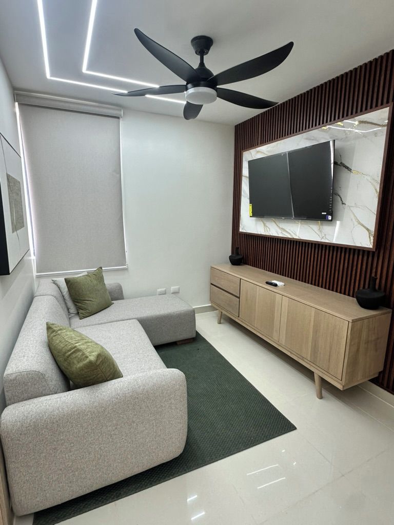 Un soggiorno moderno con un divano, una TV montata su un pannello di legno, una ventola a soffitto e una lampada da terra.