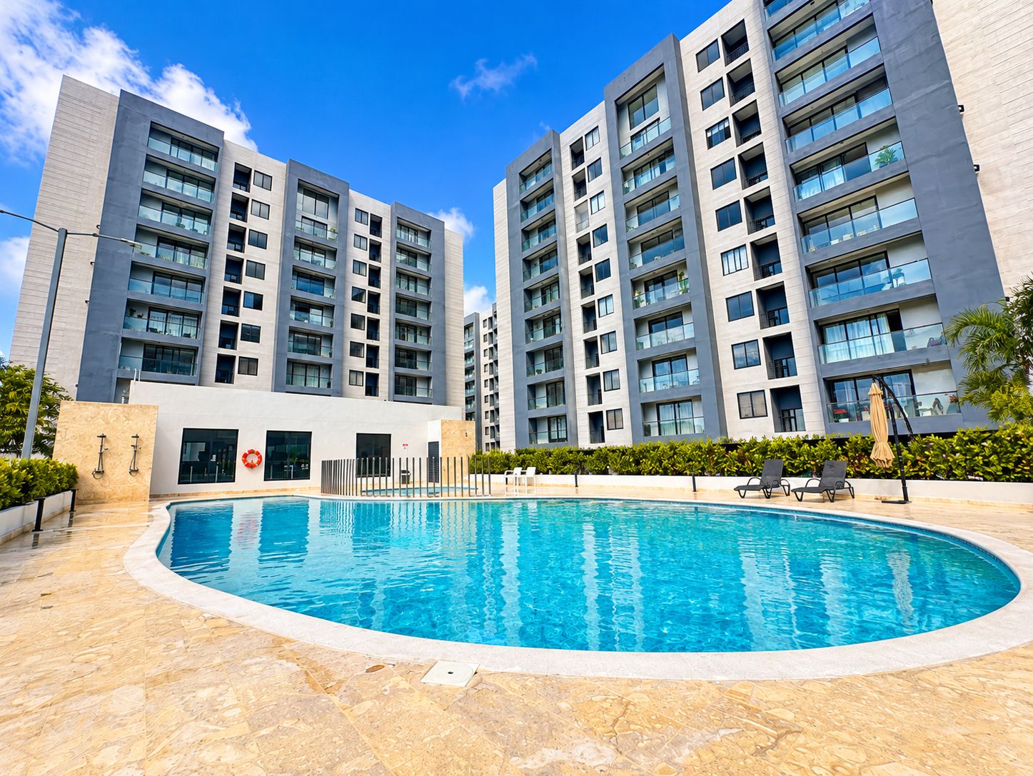 Ein modernes Gebäude mit Schwimmbad, mehreren Balkonen und blauem Himmel.