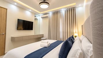 Una moderna camera d'albergo con un letto grande, una TV a schermo piatto, uno specchio, un comodino e una finestra con tende.