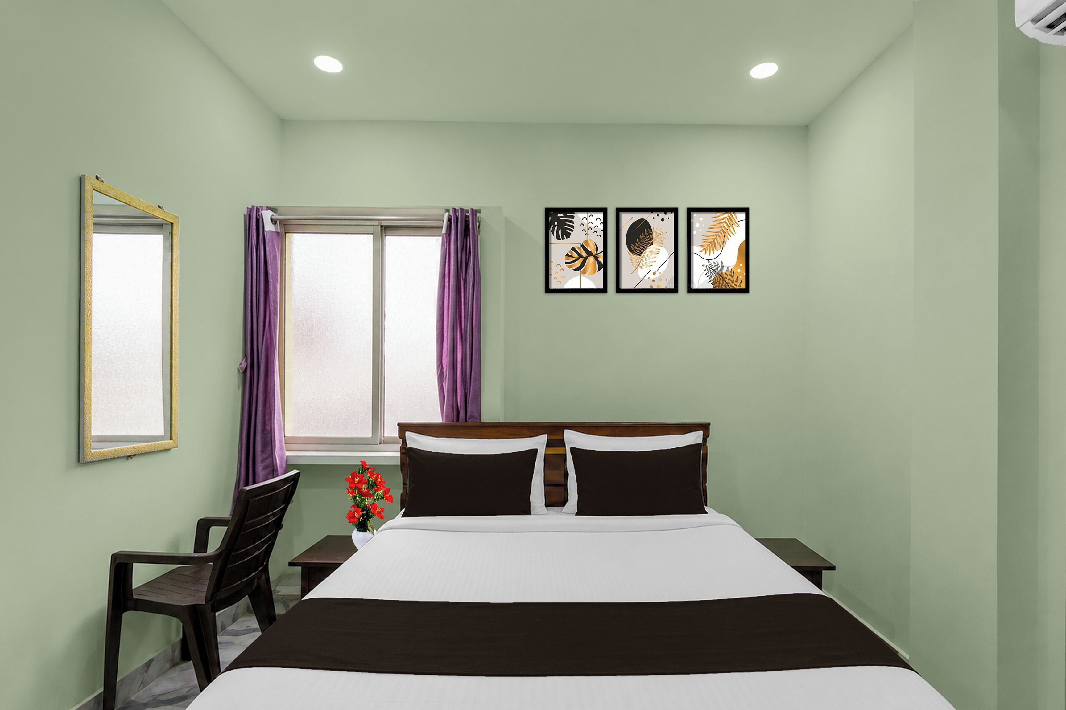 Habitación de hotel con cama, escritorio, silla, ventana con cortinas y tres cuadros en la pared.