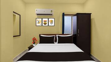 A hotel room with a bed, a wardrobe, an air conditioning unit, and three framed artworks on the wall.