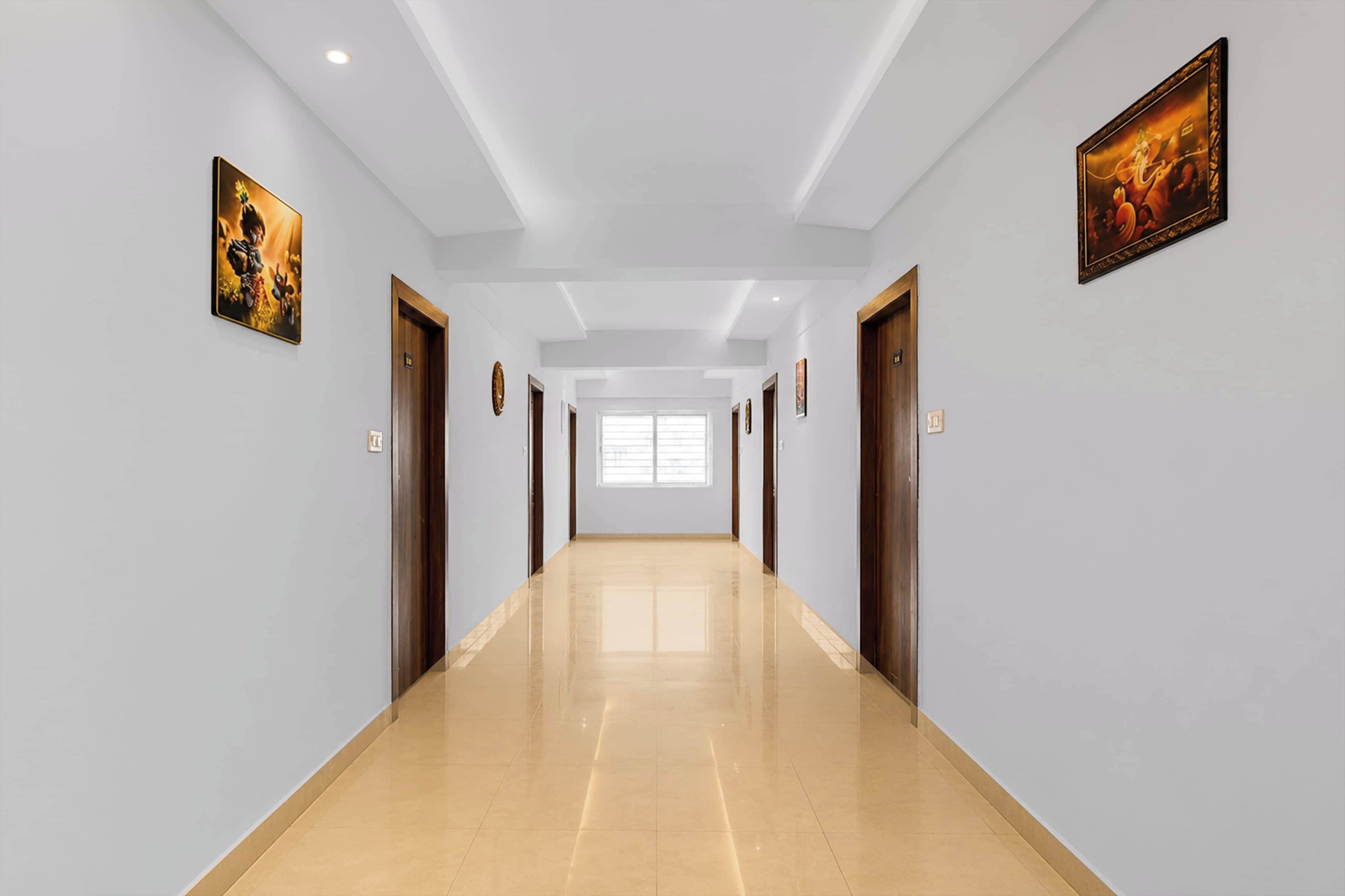 Un pasillo largo y estrecho con paredes de tonos claros y suelo brillante, que conduce a una habitación luminosa con un ventanal grande.