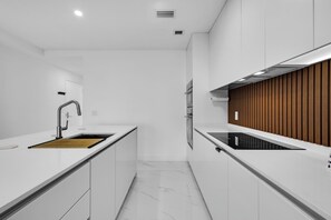 A modern kitchen with white cabinetry, a wooden countertop, a stainless steel faucet, and built-in appliances. - Azure Crown Apartment (Miami)