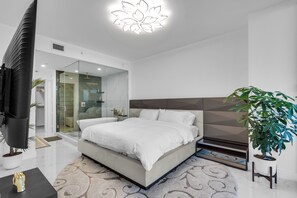 A modern bedroom with a large bed, a television, a glass shower enclosure, and a potted plant. - Azure Crown Apartment (Miami)