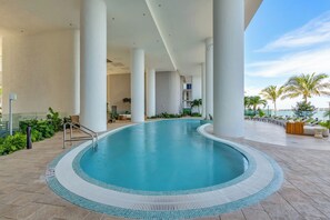 A swimming pool with a tiled edge, surrounded by lounge chairs and palm trees, with a clear view of the sky. - Azure Crown Apartment (Miami)