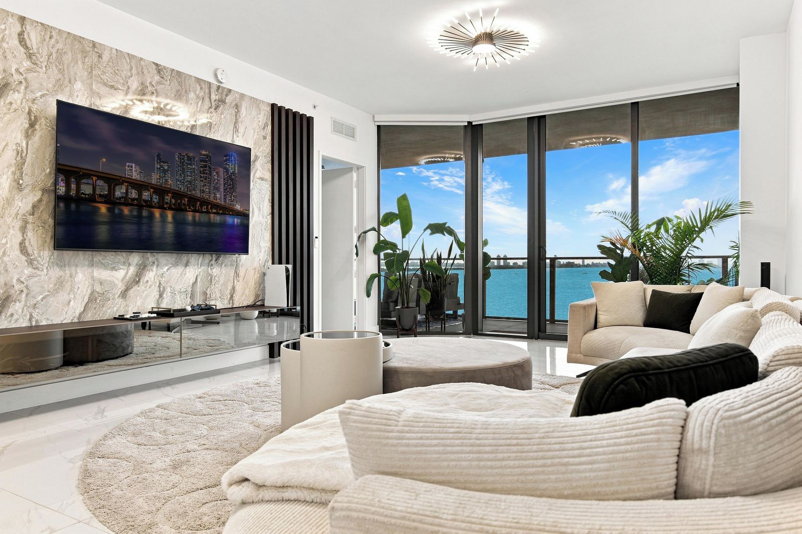 Ein modernes Wohnzimmer mit einem großen Flachbildfernseher, einer Couch, einem Couchtisch und Meerblick durch große Fenster.