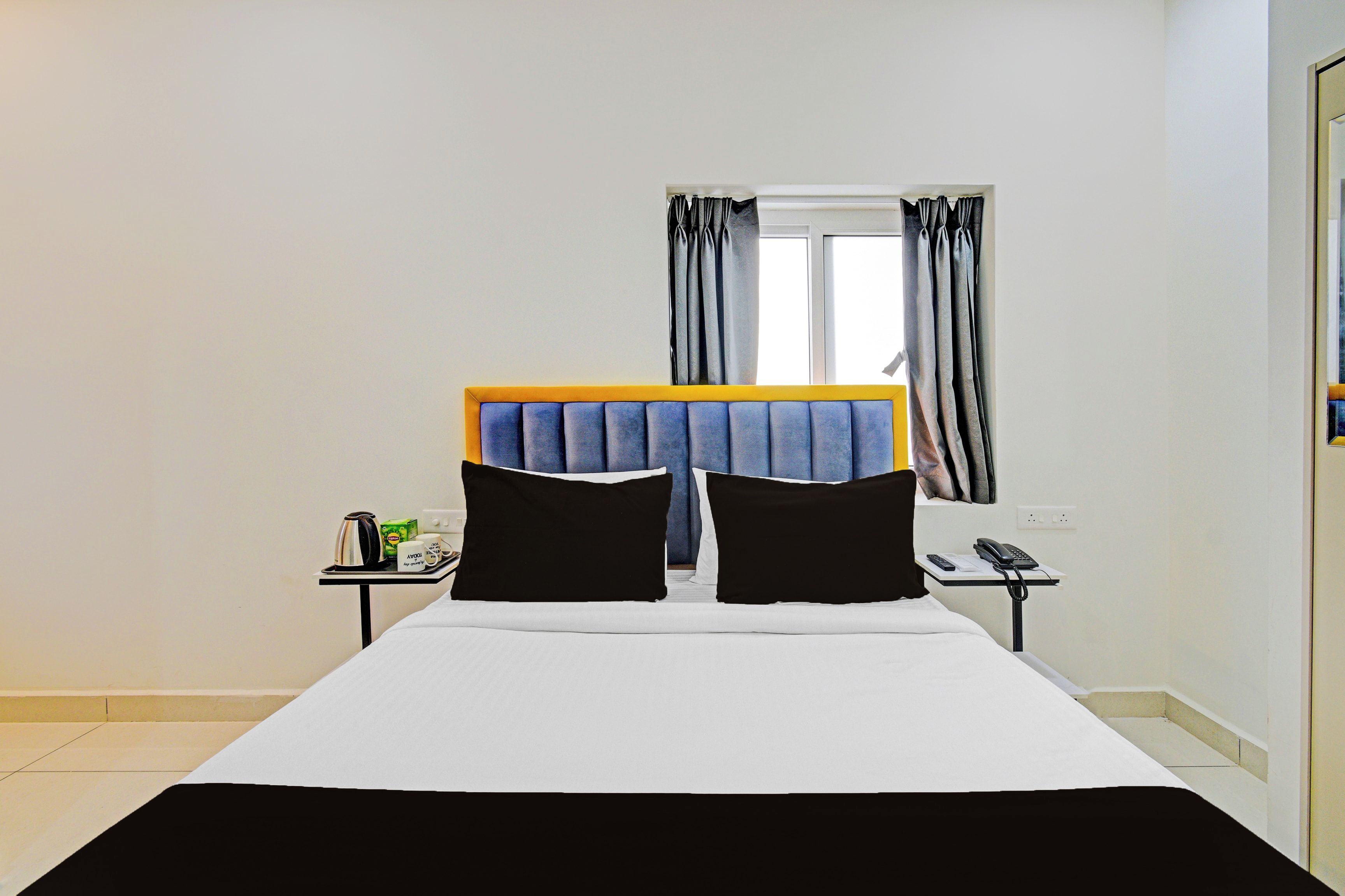A hotel room with a bed, a bedside table, a nightstand, a window with curtains, and a door.