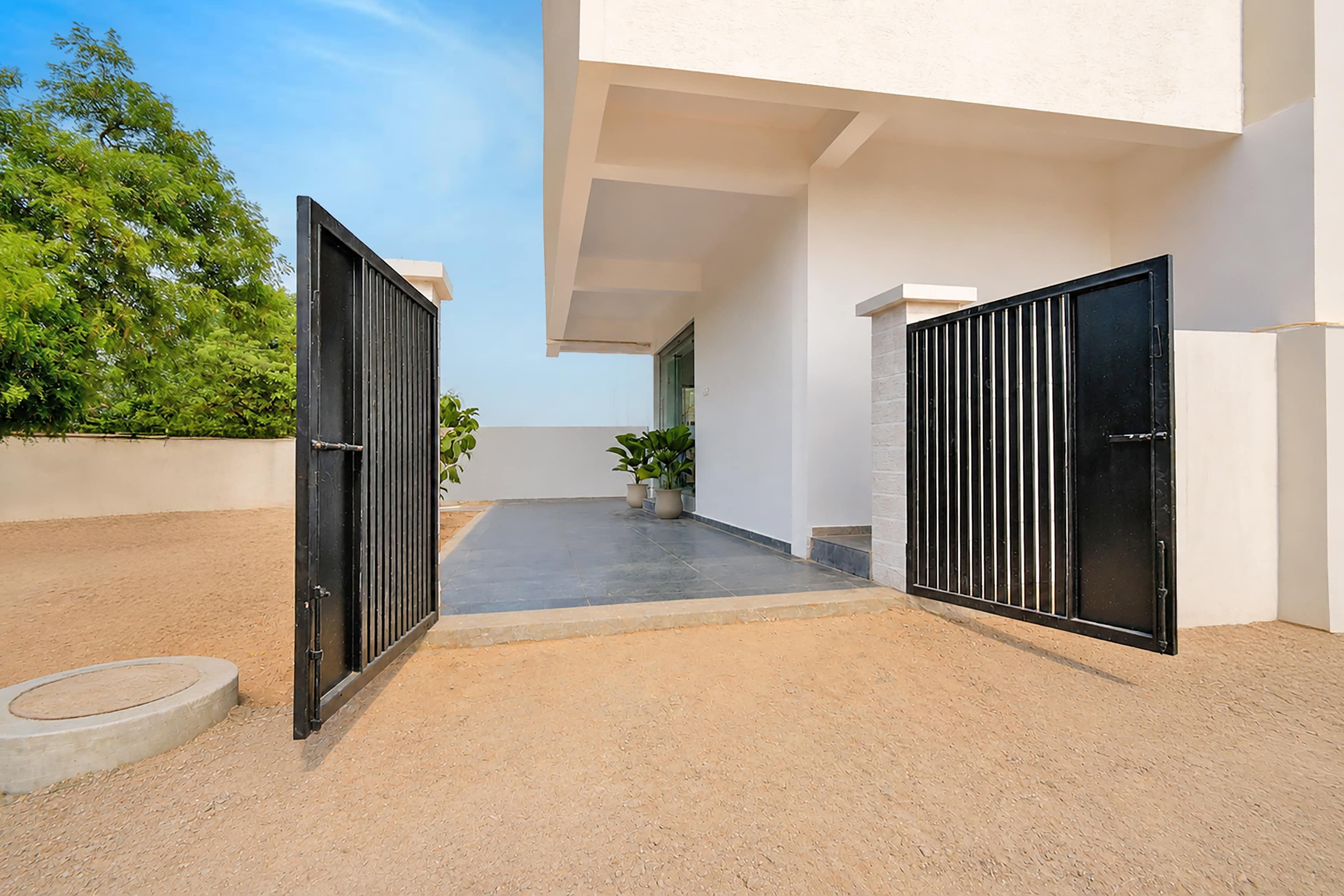A modern building with two black gates, a paved courtyard, and potted plants.