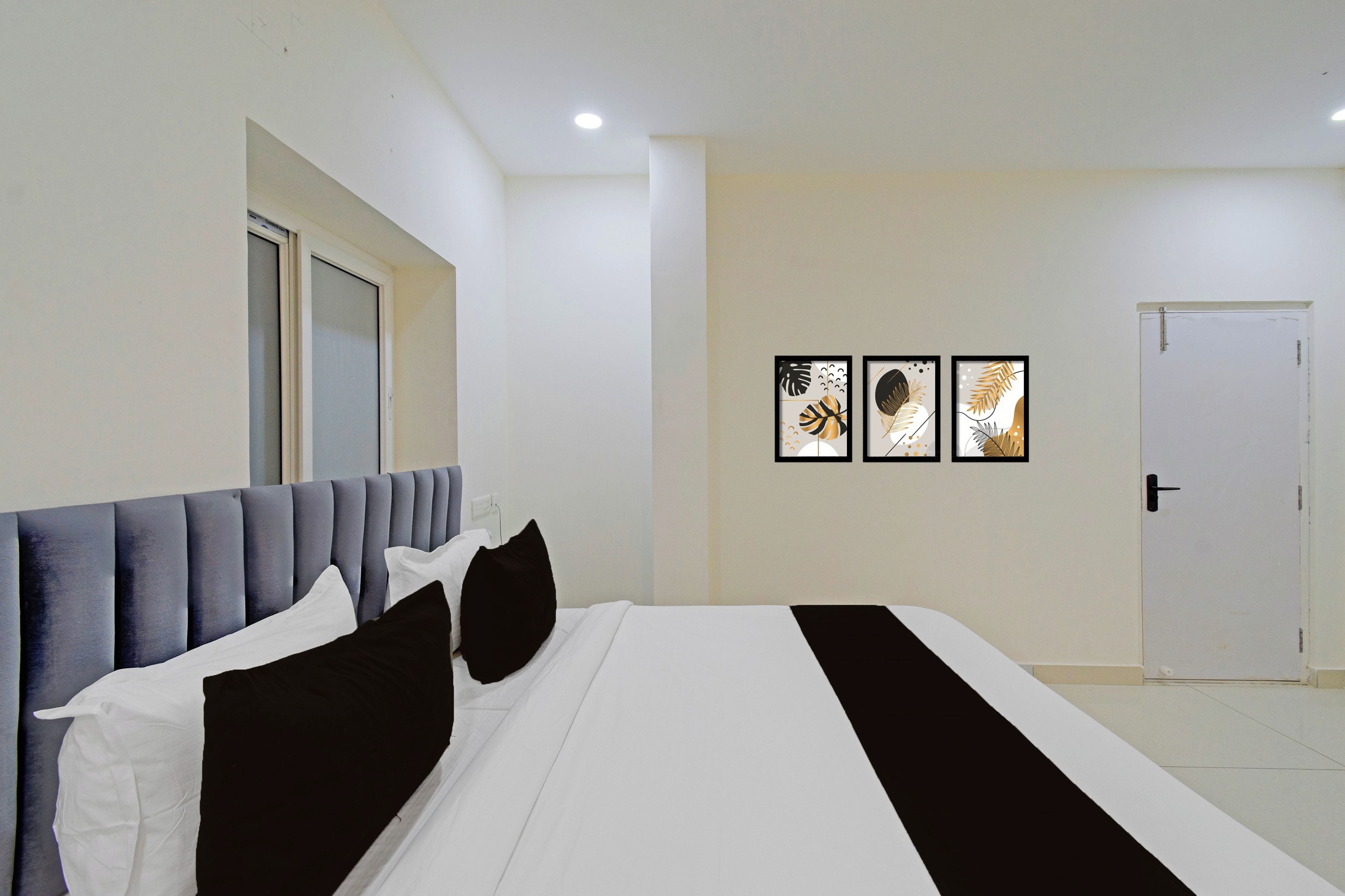 A hotel room with a bed, a door, and three framed pictures on the wall.