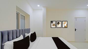A hotel room with a bed, a door, and three framed pictures on the wall.