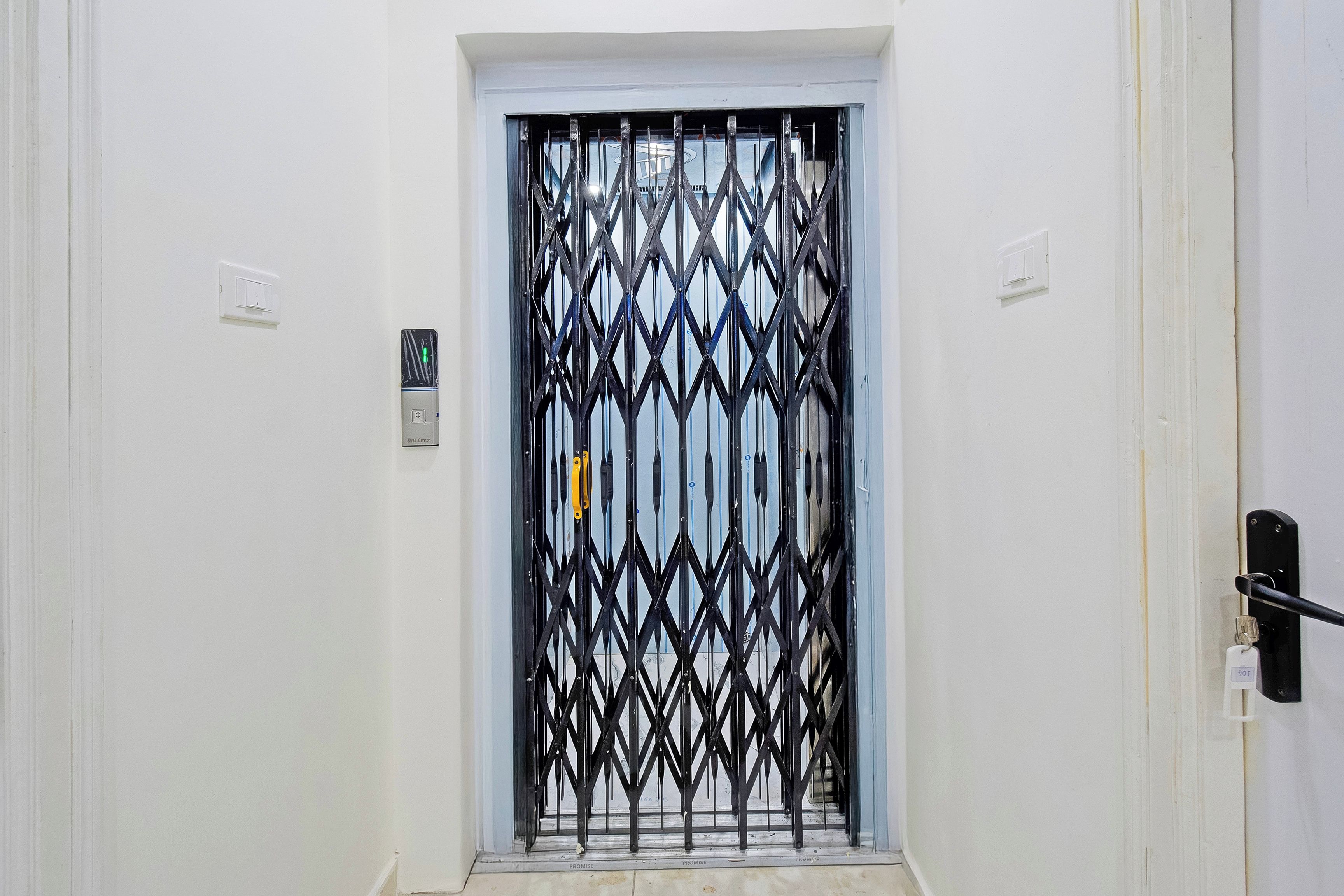 A door with a black metal security gate, a light switch, and a keycard reader on the wall.