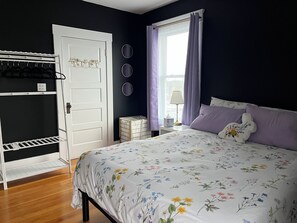 A bedroom with a bed, a wardrobe, a window with curtains, and a bedside table with a lamp.