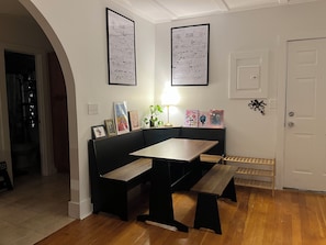 Una habitación con un banco y una mesa de madera, obras de arte enmarcadas en las paredes, una planta en maceta y una puerta.