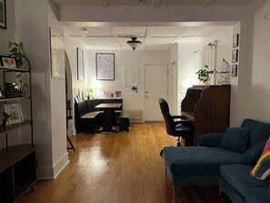 A living room with a blue sofa, a wooden coffee table, a dining area with a bench, and a piano.