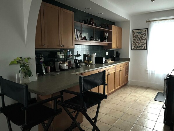 A modern kitchen with wooden cabinets, a black countertop, and a dining area with two black chairs.