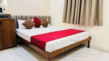 Una cama bien hecha con estructura de madera, colcha roja y varias almohadas.