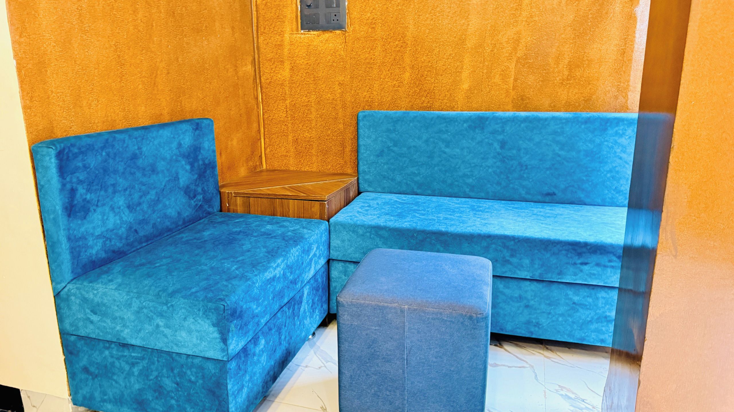 Una stanza angolare con un divano blu, un poggiapiedi coordinato e un tavolino in legno.
