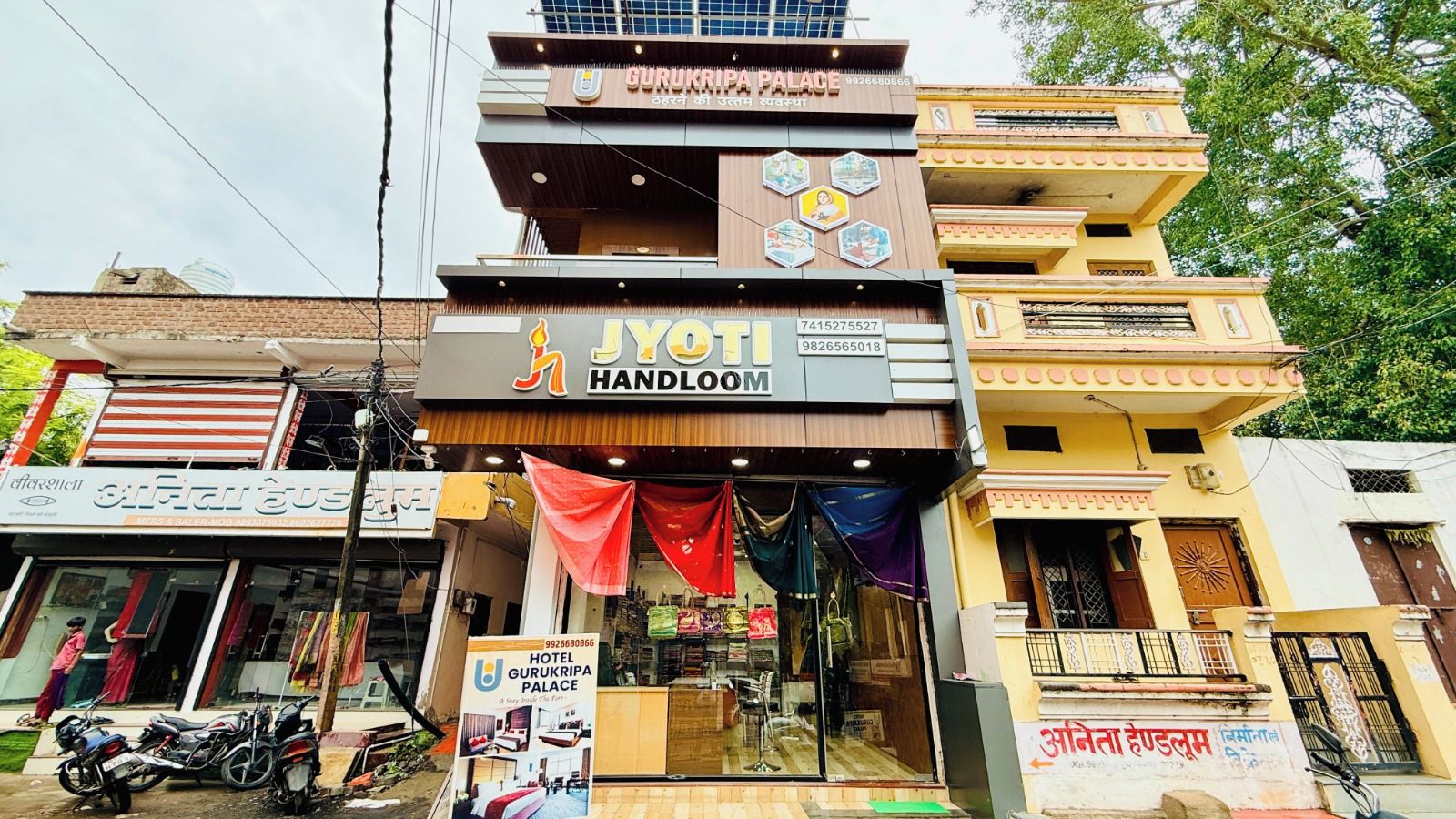 A multi-story building with a prominent sign for 'Gurukripa Palace Hotel' and a storefront named 'JYOTI HANDLOOM' below it.