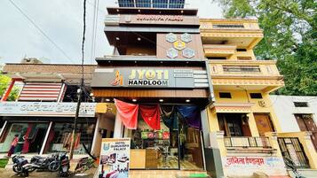 A multi-story building with a prominent sign for 'Gurukripa Palace Hotel' and a storefront named 'JYOTI HANDLOOM' below it.