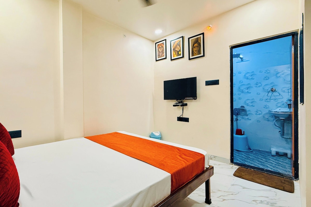Habitación de hotel con cama, televisión y baño visible a través de una puerta de vidrio.