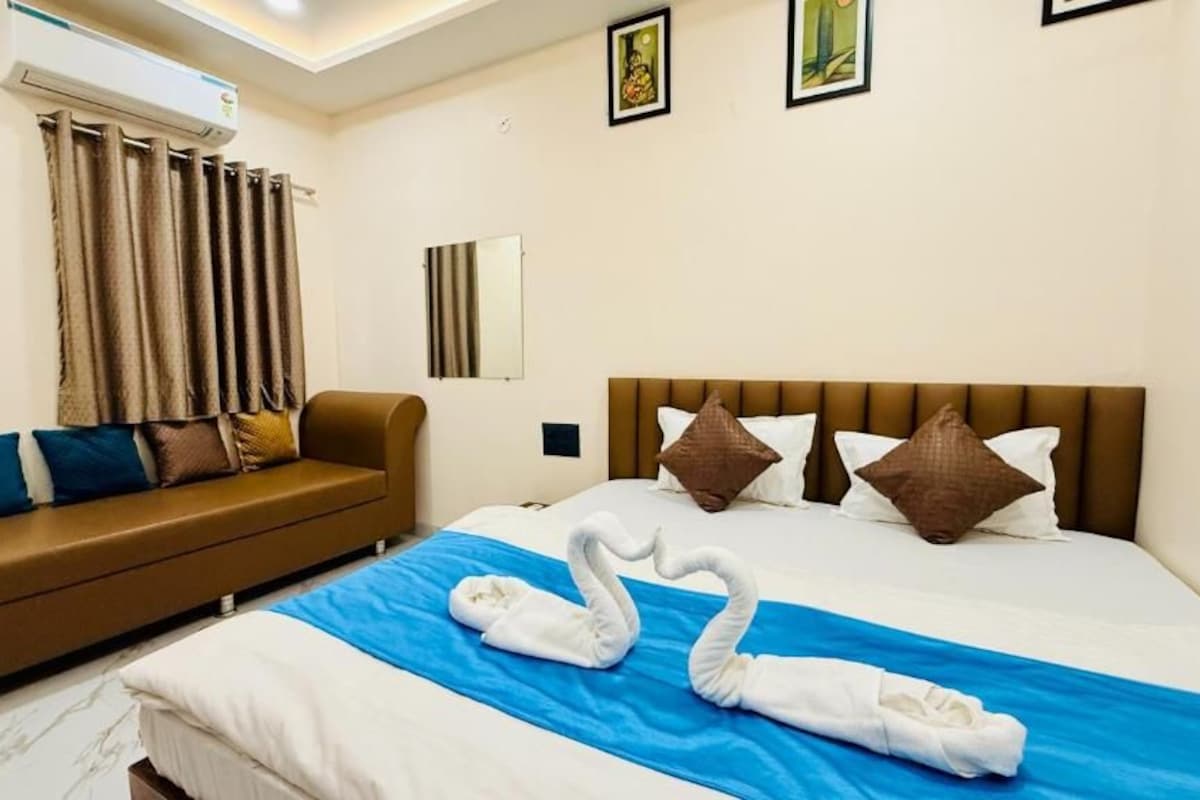A hotel room with a bed, a sofa, a blue bedspread, and a swan-shaped towel arrangement.
