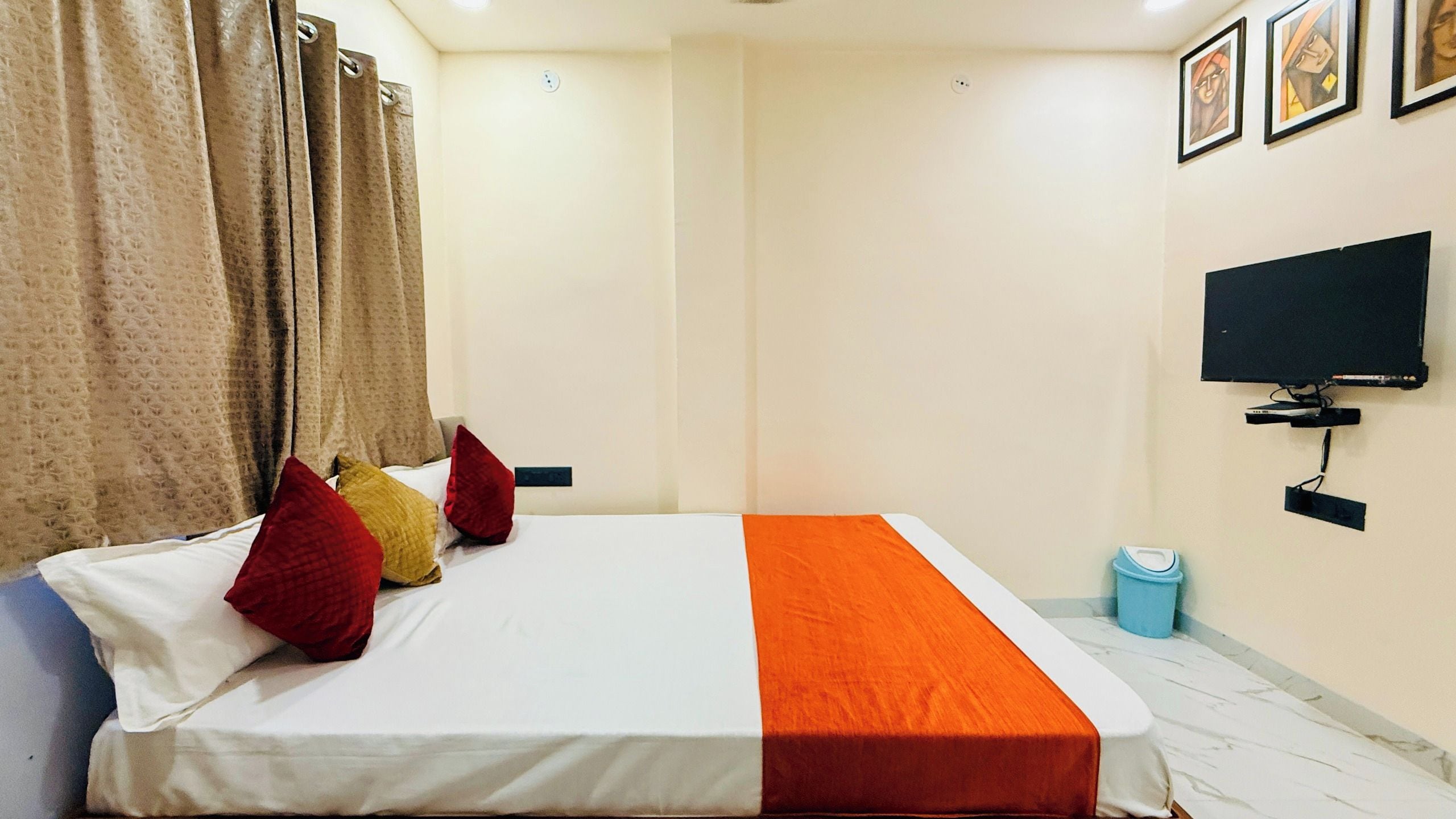 A hotel room with a bed, curtains, a television, and a trash bin.