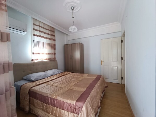 A bedroom with a bed, a wardrobe, an air conditioning unit, and a door.