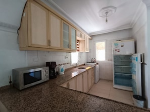 Una cocina con armarios de madera, microondas, cafetera, lavaplatos y refrigerador.
