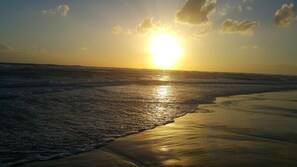 A beach with waves and the sun setting in the background.
