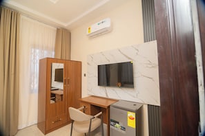 Habitación de hotel con armario de madera, escritorio, silla, televisor montado en una pared de mármol y minibar.