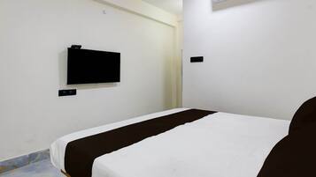 Habitación de hotel con una cama individual, un televisor de pantalla plana montado en la pared y un pequeño equipo de aire acondicionado sobre la cama.