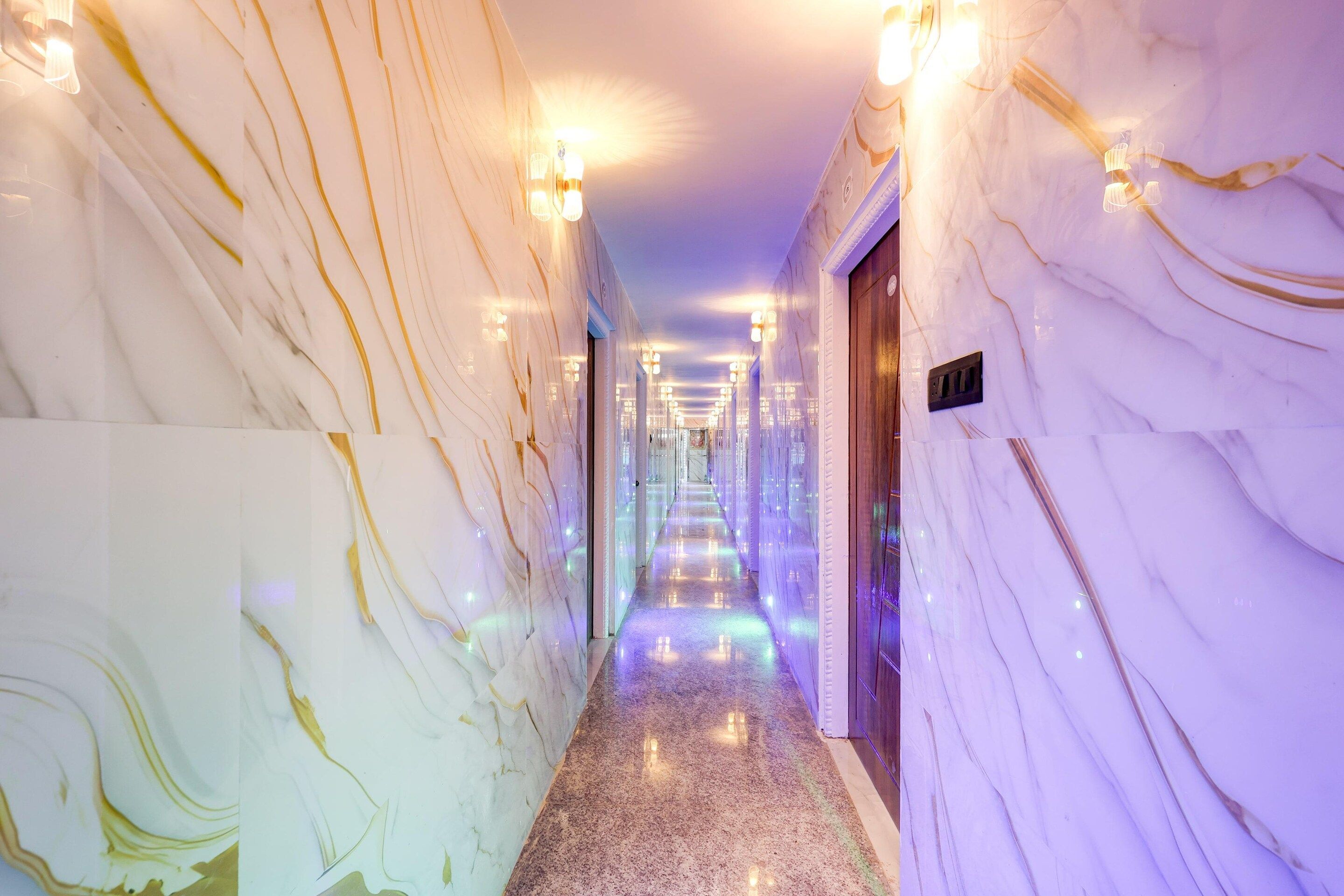 A marble-lined hallway with wall sconces and a door at the end.