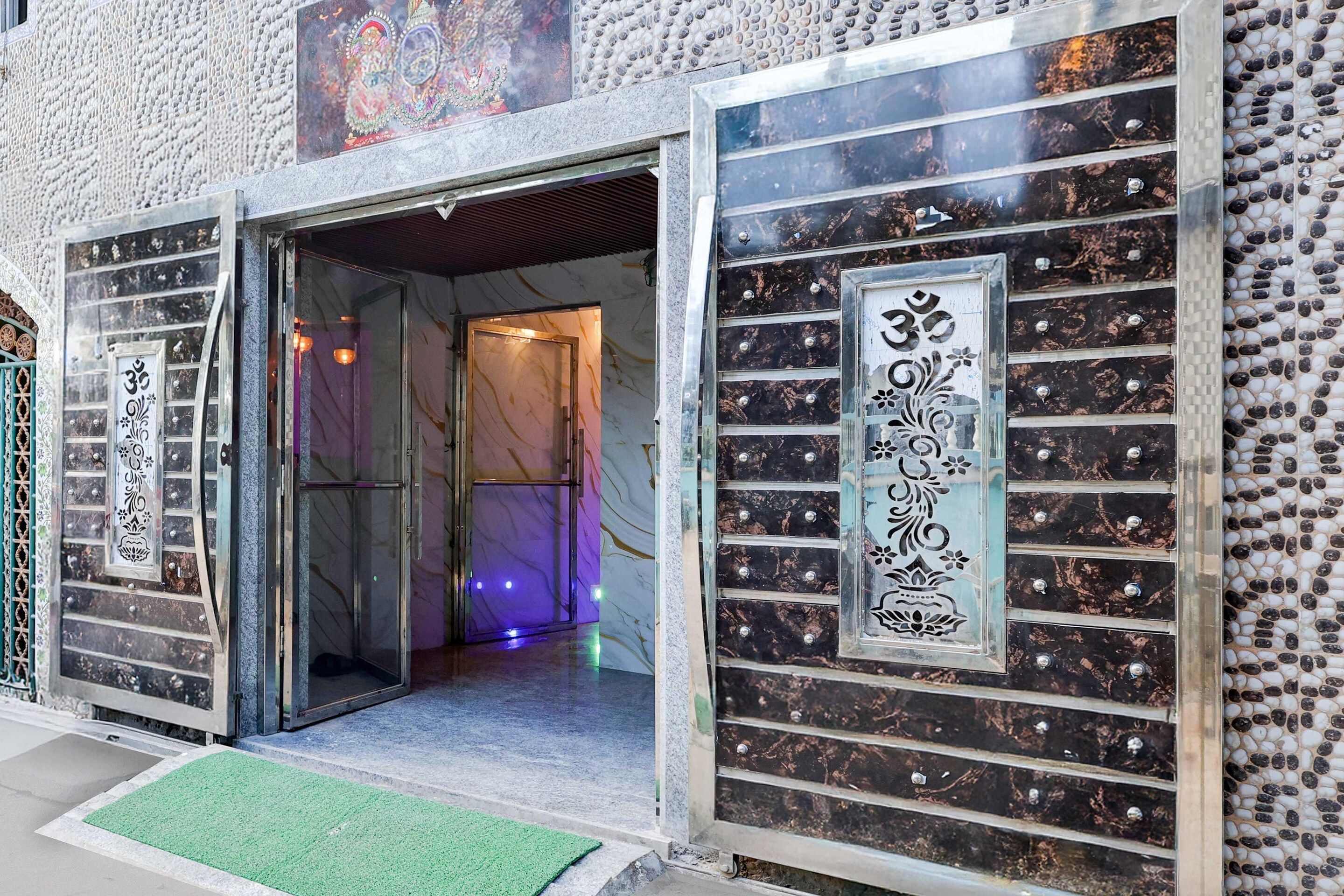 Entrada de un edificio con puerta de cristal, felpudo verde y paneles decorativos con inscripciones.