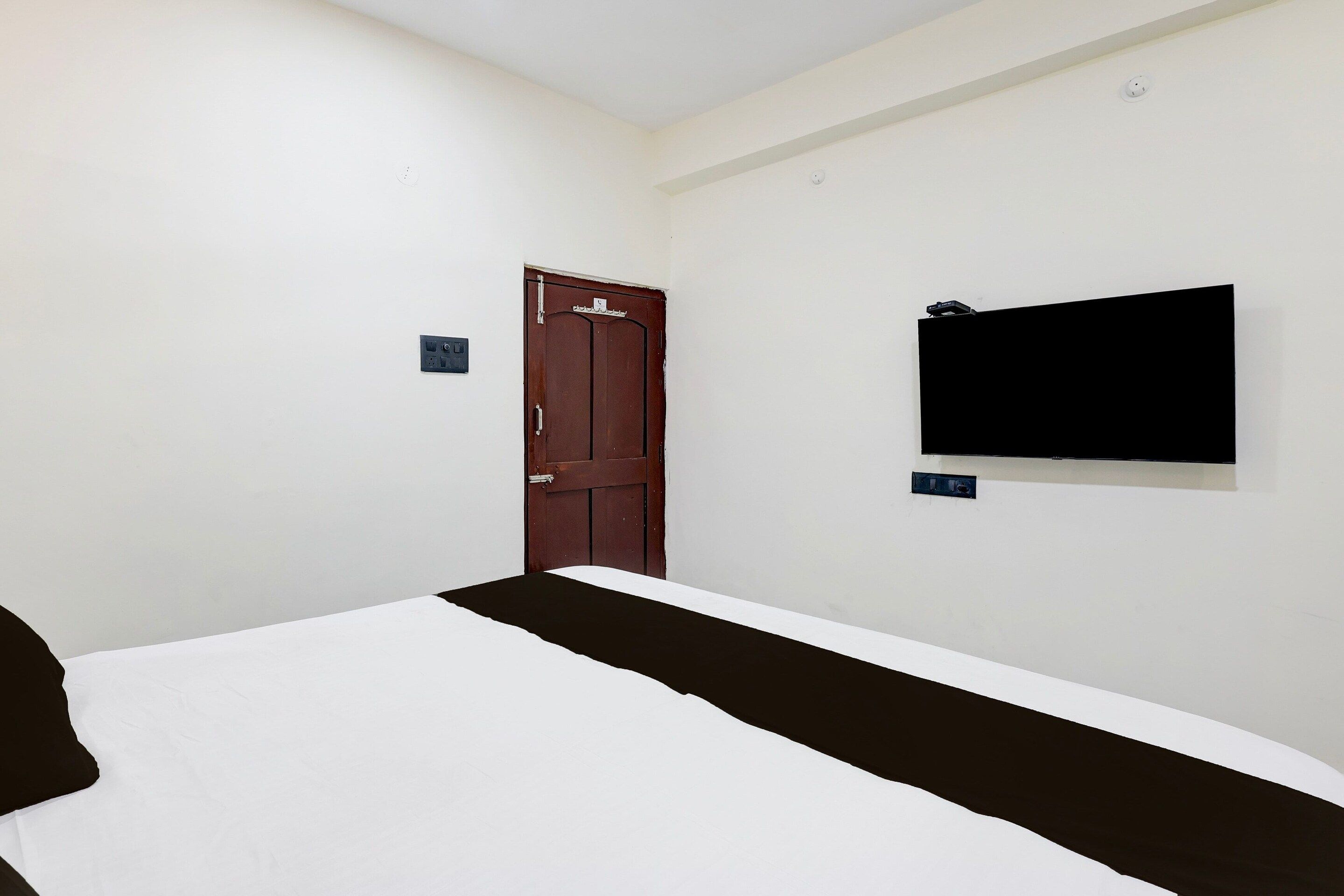 Een eenvoudige kamer met een bed, een deur en een aan de muur bevestigde televisie.