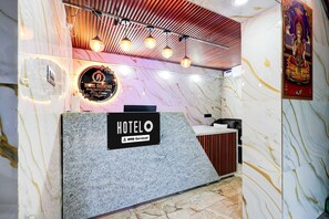 Un hall d’hôtel avec un mur en marbre, un comptoir d’accueil et un plafond orné de poutres apparentes et de luminaires suspendus.