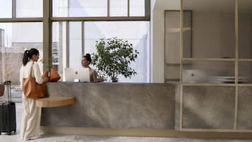 Un comptoir d’accueil avec un ordinateur portable, une plante en pot et une valise.