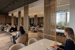 Un comedor moderno con separadores de madera, mesas de mármol y vistas al exterior.