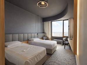 Habitación de hotel con dos camas, un escritorio, una silla y un ventanal con vistas a la ciudad.