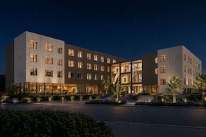 Un hotel moderno con varios pisos, amplias ventanas y una entrada bien iluminada.