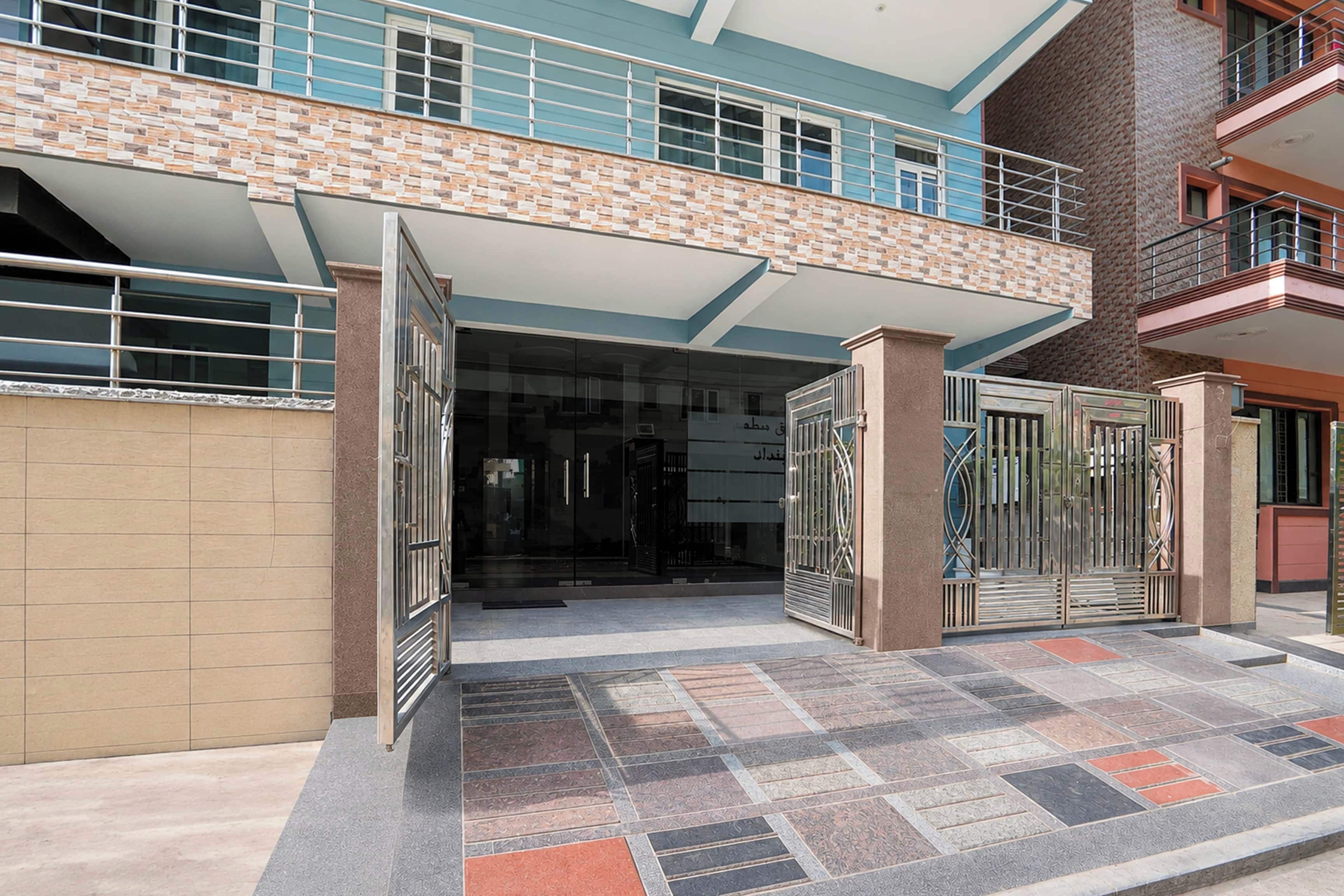 Una entrada de edificio con suelo de baldosas, puerta de cristal y reja metálica.