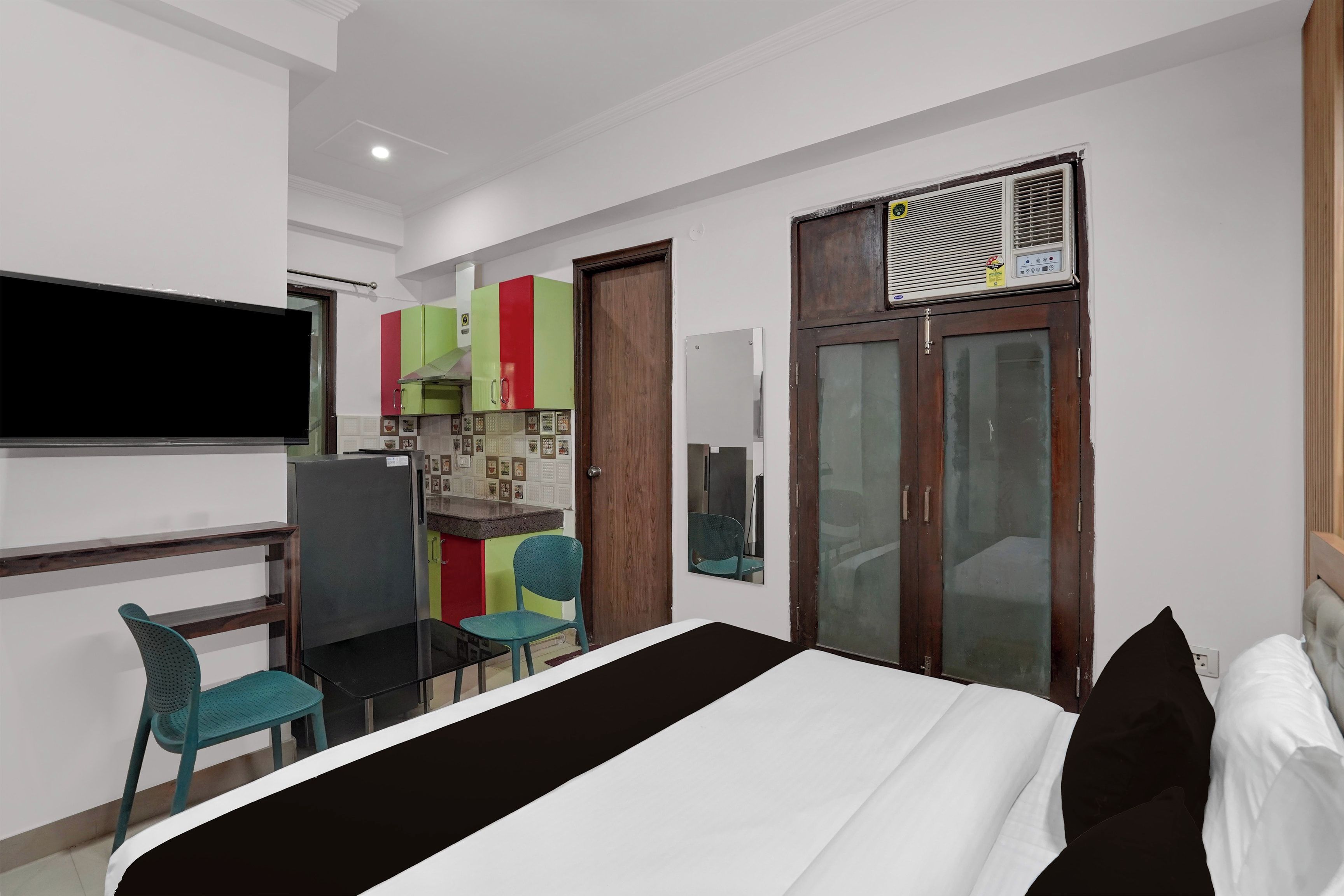 A hotel room with a bed, a desk, a chair, a TV, a wardrobe, and a bathroom with a mirror.