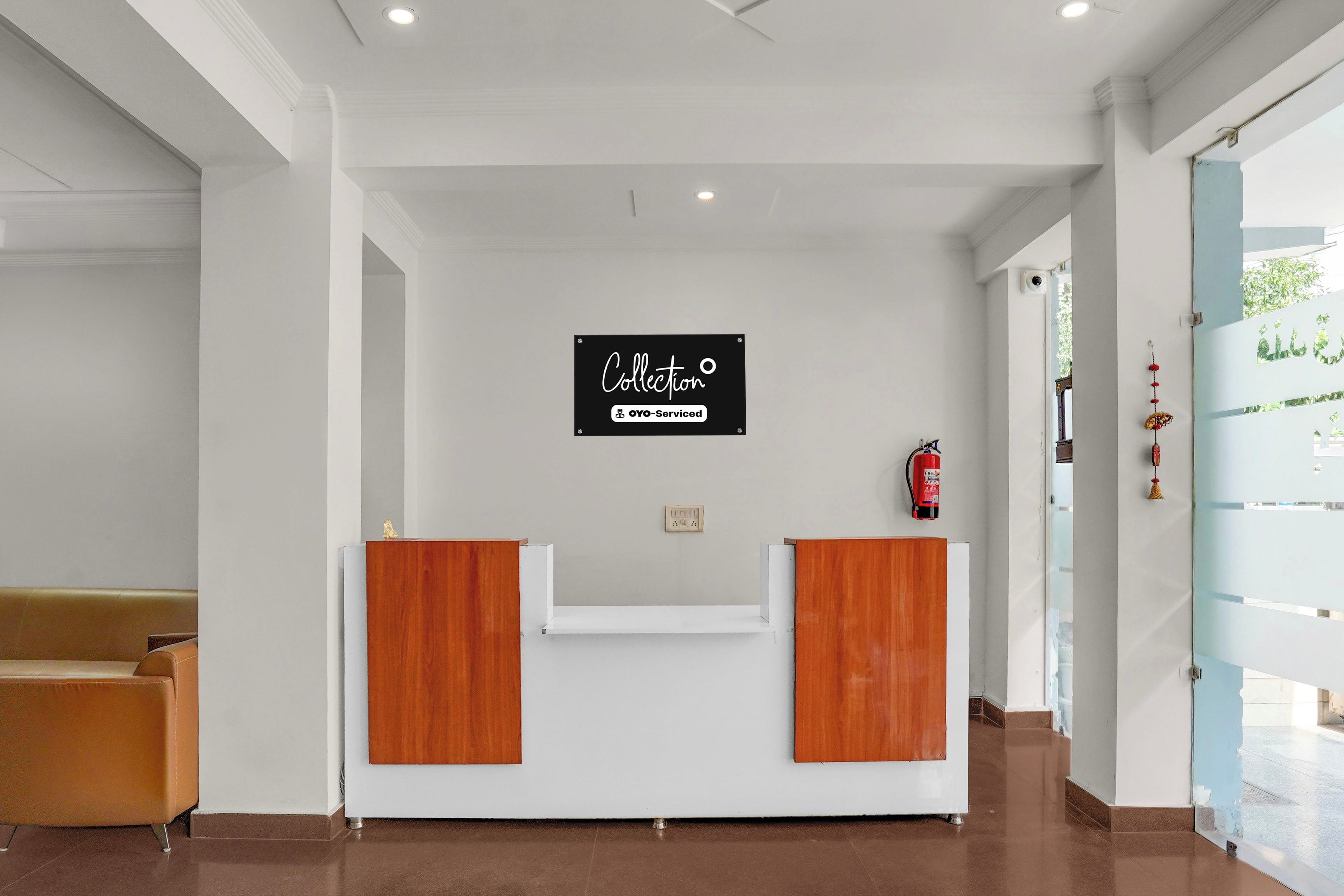 A reception desk with a sign indicating it's serviced by OYO, a reception area with a bench, and a fire extinguisher on the wall.