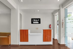 Balcão de recepção com placa indicando serviço OYO, área de espera com um banco e um extintor de incêndio na parede.