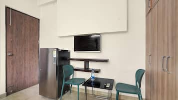A small kitchenette with a refrigerator, a microwave, and a water dispenser. There is a television mounted on the wall above a small table with two chairs.