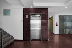 Un ascensor modern amb acabat metàl·lic, una paret decorativa de marbre i un extintor de foc fixat a la paret.