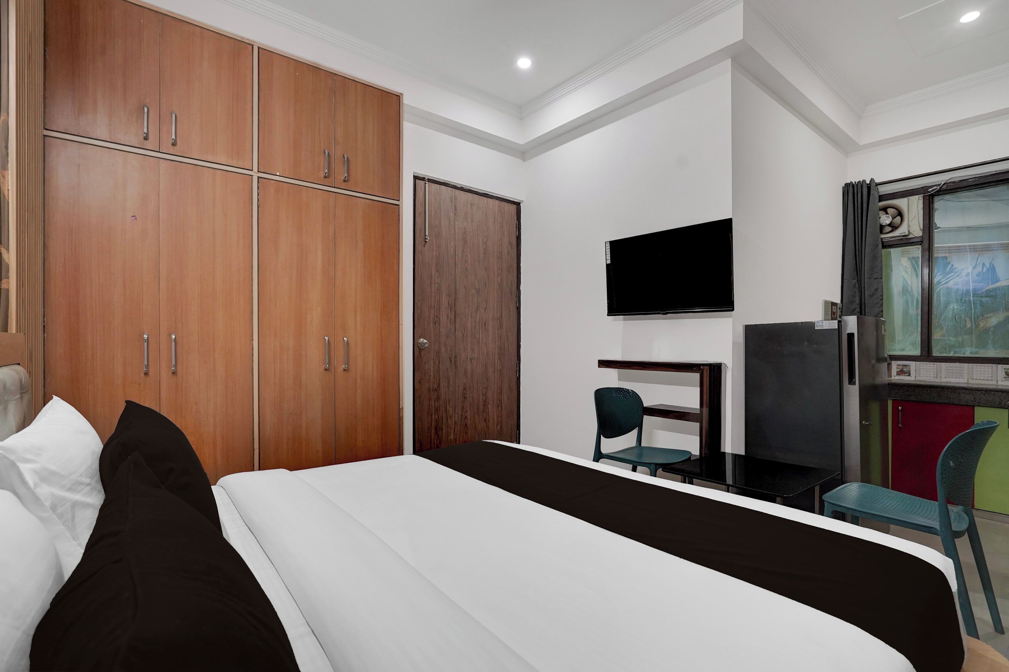 Quarto de hotel com cama, televisão, escrivaninha e guarda-roupa.