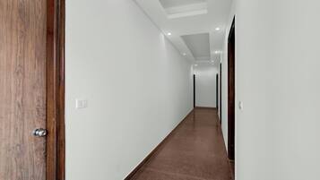A long, narrow hallway with white walls and a brown carpet. There are doors on both sides, and the hallway is well-lit with ceiling lights.