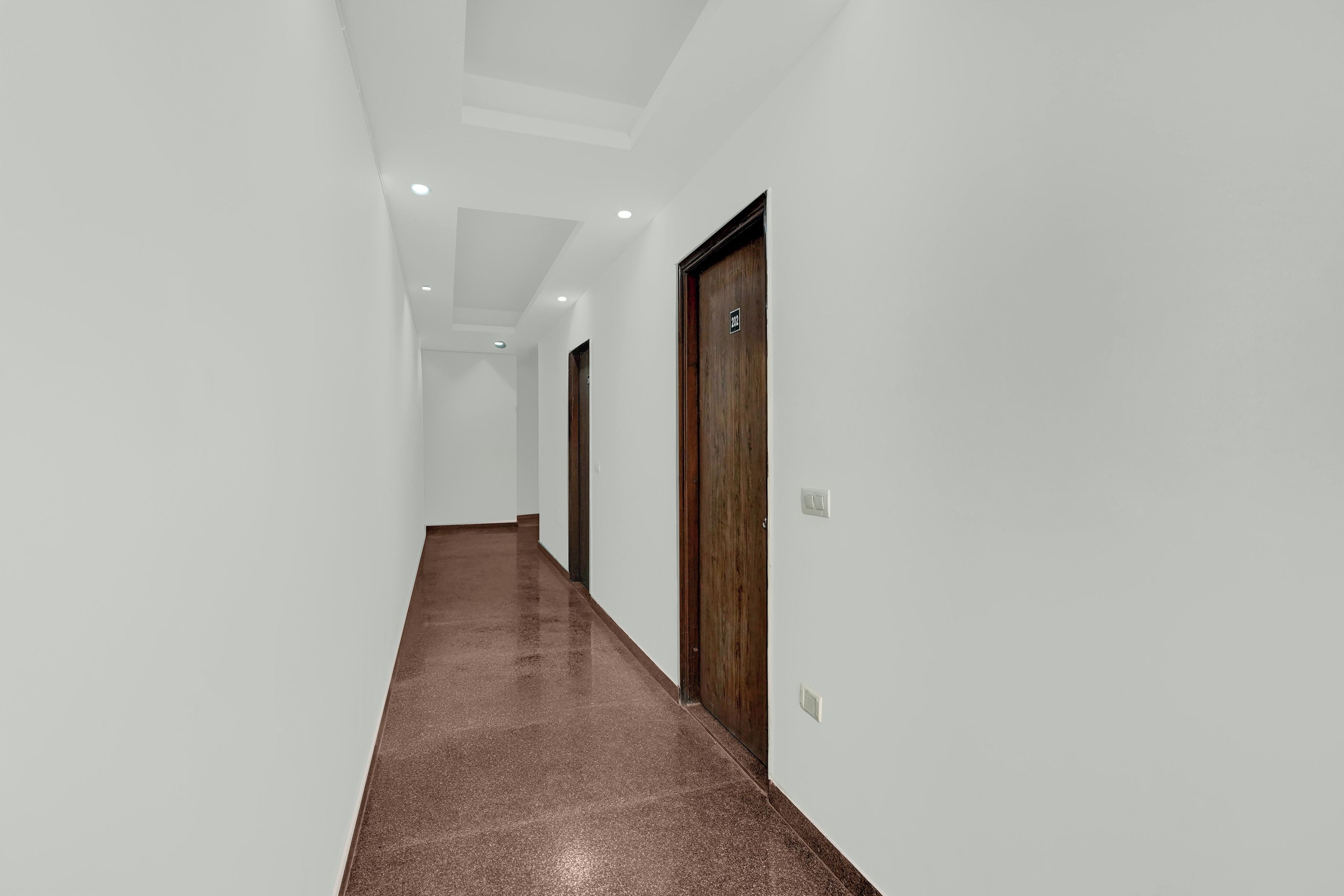 Un couloir aux murs blancs, avec un tapis marron et une porte en bois portant une plaque avec un numéro.