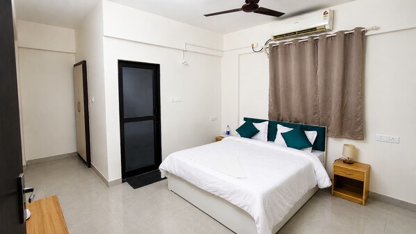 Habitación de hotel con cama, mesita de noche, ventilador de techo, aire acondicionado y una puerta.