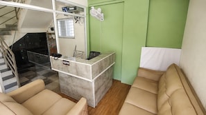 Una mesa de recepción con un cartel que dice 'RECEPTION', una silla, un ventilador y una escalera que sube a un nivel superior.